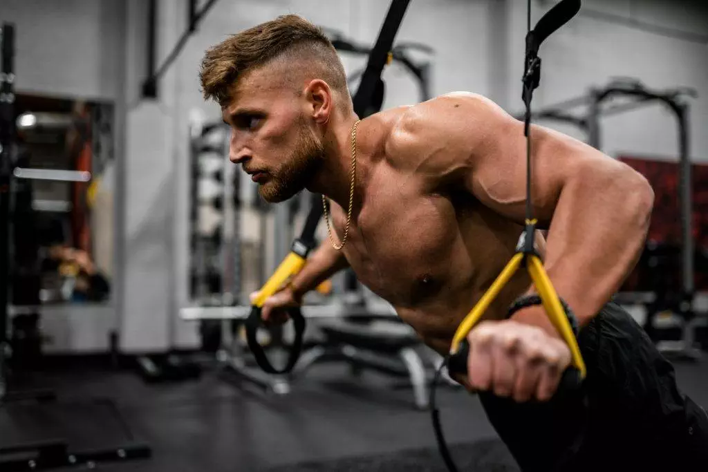 topless man in black pants holding black and yellow exercise equipment